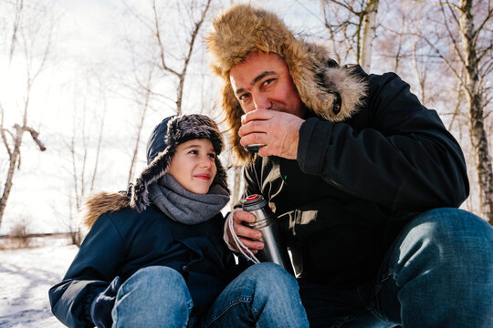 Father drinking tea sitting next to son in winter