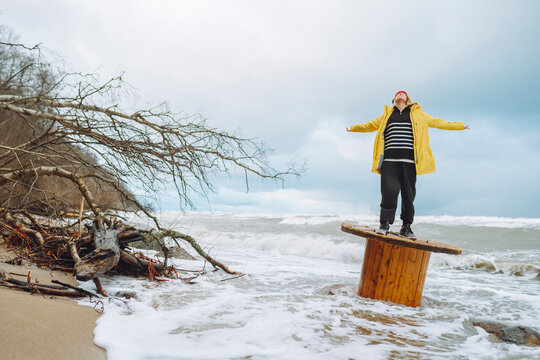 Carefree woman standing with arms outstretched on wooden spool at beach