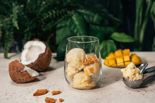 Mango and coconut ice cream in glass near serving scoop