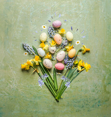 Easter flowers bunch with springtime flowers and colorful eggs on green background, top view