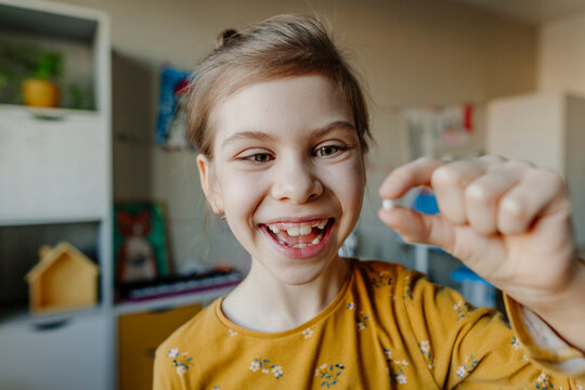 Cheerful girl holding broken tooth at home
