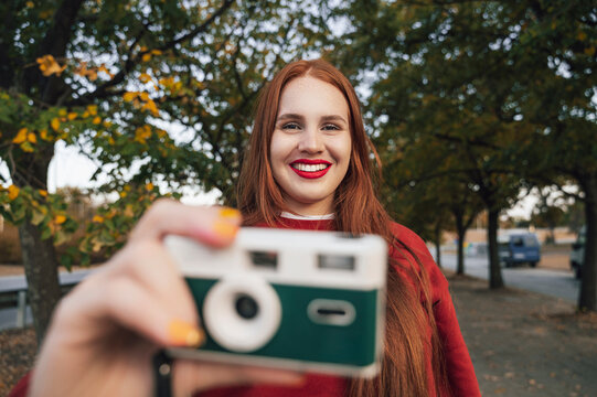 Redhead woman holding camera at autumn park