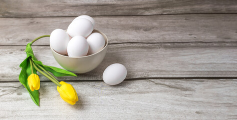 White eggs lie in a ceramic bowl with tulips