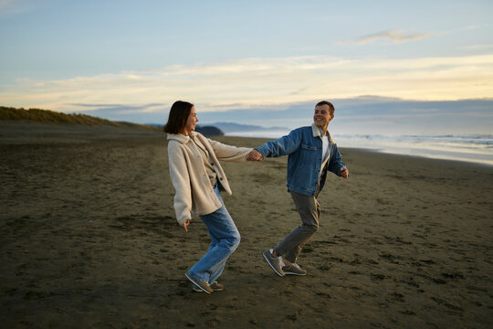 Smiling man holding hand of girlfriend and walking on beach