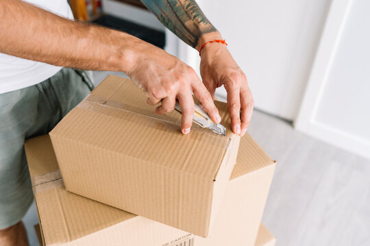Hands of man opening cardboard box with utility knife at new home
