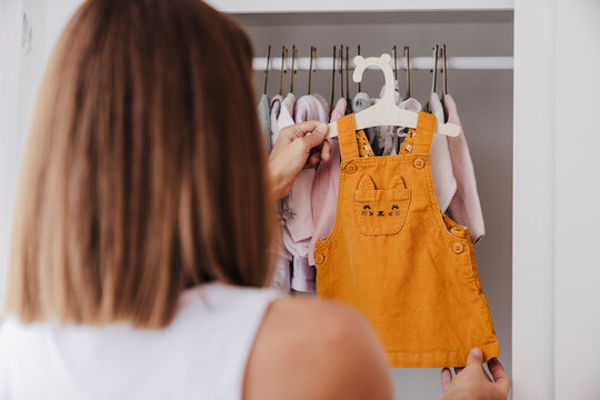 Woman holding baby clothes near closet at home
