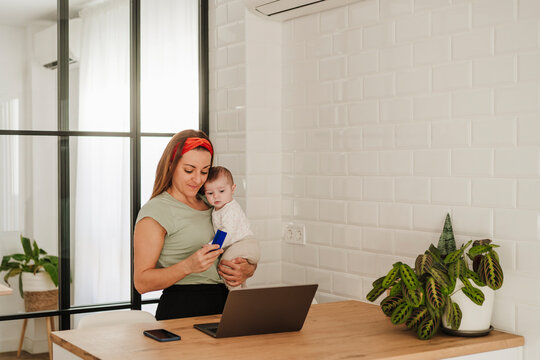 Woman carrying baby girl and doing online shopping on laptop at home