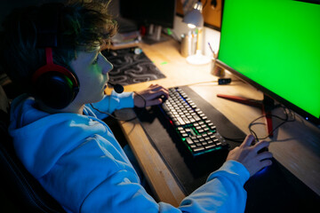 Boy wearing headset and playing video game on computer at home