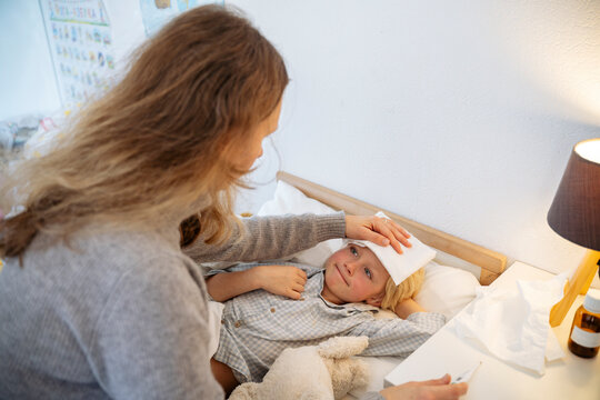 Mother putting compress on son's forehead lying on bed at home