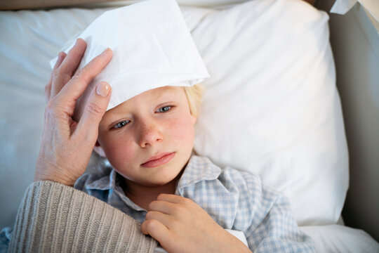 Thoughtful sick boy with white compress on forehead at home