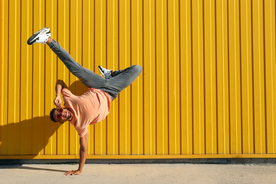 Carefree man doing hand stand in front of yellow striped wall