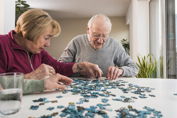 Home caregiver playing puzzle game with senior couple