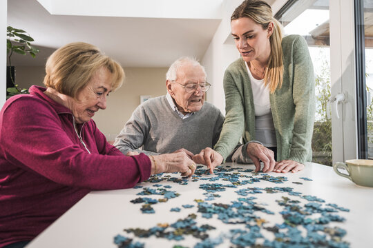 Home caregiver with senior couple playing puzzle at table
