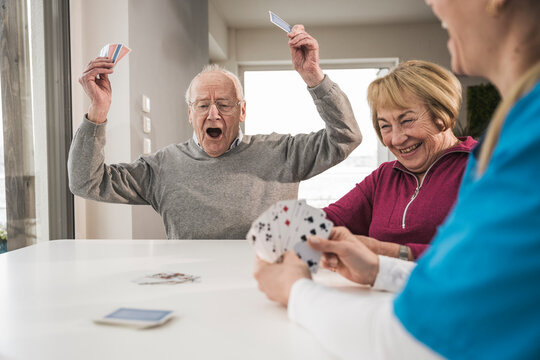 Cheerful man playing cards with woman and home caregiver at table