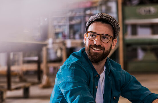 Smiling carpenter wearing eyeglasses and flat cap at workshop