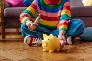 Woman sitting with hammer and piggy bank at home