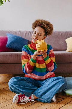 Happy young woman sitting with piggy bank