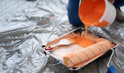 Close-up of orange paint pouring into tray. Tools for the painter and redecoration