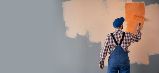 painter man at work with a paint roller painting wall in orange colour. Home renovation concept. Banner.