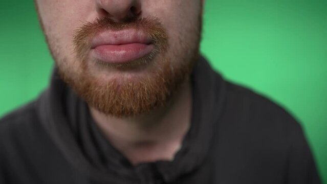 a close-up of the man's lips with which he performs beatbox-like movements. a man with a red beard moves his lips while letting out air. male lips close up. shooting on a green background.