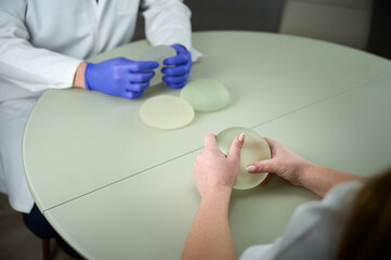 Close-up of female plastic surgeon demonstrates breast implants to a patient for her new breast....