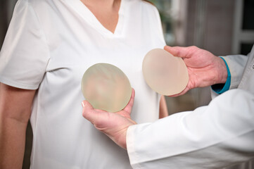 Close-up of female plastic surgeon demonstrates breast implants to a patient for her new breast. The plastic surgeon holds breast silicone implants. Breast augmentation concept. Breast Implant Samples