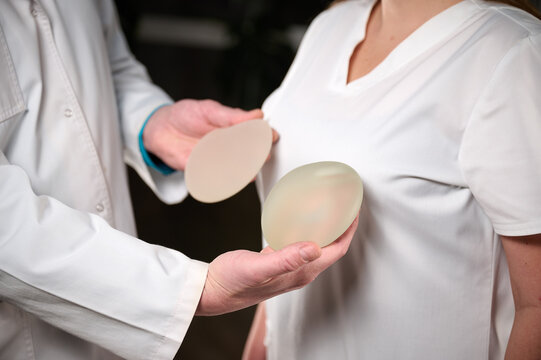 Close-up of female plastic surgeon demonstrates breast implants to a patient for her new breast. The plastic surgeon holds breast silicone implants. Breast augmentation concept. Breast Implant Samples
