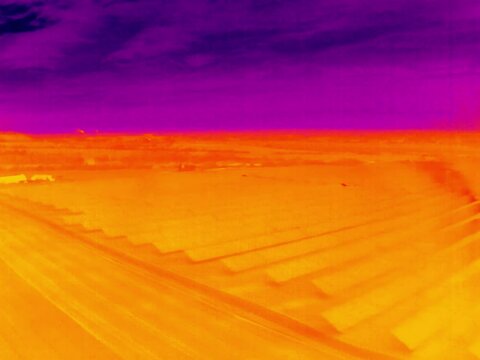 Aerial infrared thermal view of solar power plant on large photovoltaic farm, in purple and yellow hues
