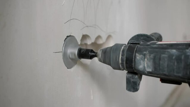 Electrician using rotary hammer and diamond core drill to create socket holes in wall. Professional installation for electrical outlets.