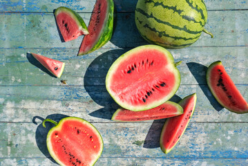 Ripe juicy watermelons and pieces of watermelon on a blue wooden table. Hard light.