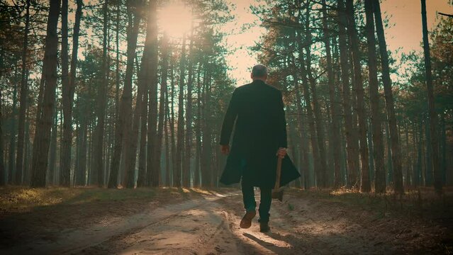 Ominous Figure Holding Axe, Murderer Walking Away Through Forest at Dusk. Bloodthirsty criminal maniac carrying case, searching for victim
