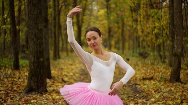 Portrait of a ballerina in a pink petticoat in the middle of a large yellow forest. Her graceful hands, curves of the body emphasize femininity. High quality 4k footage