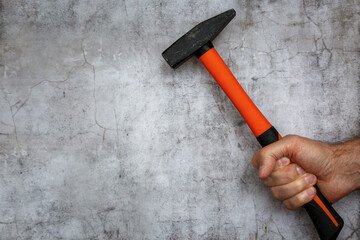 A man's hand holds a hammer against the background of a concrete wall. Cope space.