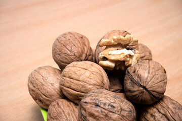 Cracked Walnut Showcasing Kernel Amidst Whole Ones, This image beautifully captures a group of whole walnuts, with one cracked open to reveal the kernel. The walnuts are placed