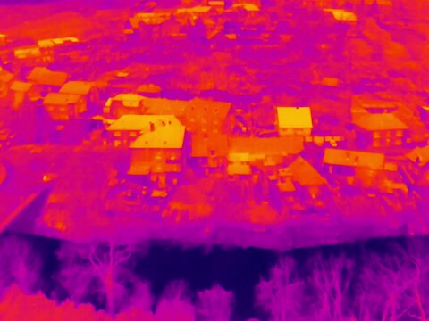Aerial infrared thermal view of river in residential area with residential buildings and houses, in purple and yellow hues
