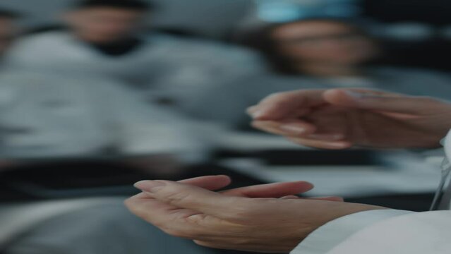 Vertical close up shot of hands of female speaker gesticulating during presentation in front of audience on health conference