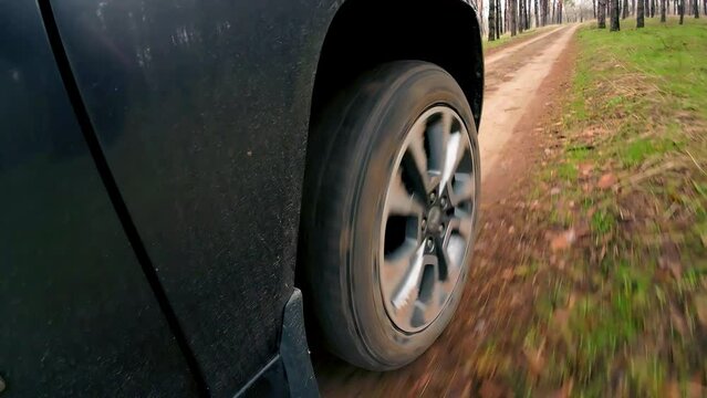 Car driving by deep terrain in forest. Close up view on spinning tires. Rotating tyre on dirty road. Automobile offroad