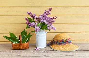 Spring rustic still life with a bouquet of lilacs, lilies of the valley in a basket and a straw hat on a garden bench. Gardening as a hobby  and pleasure