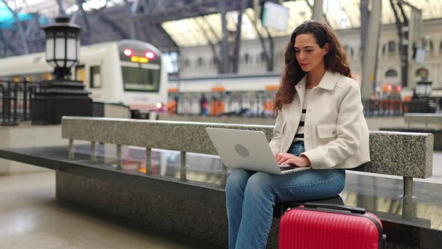 Young adult business woman working on laptop while waiting the train at station. Travel and businesspeople lifestyle concept 