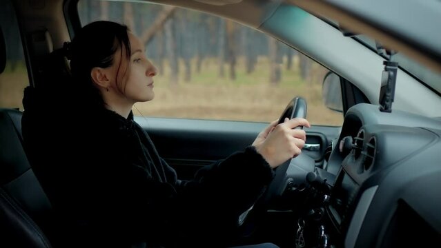 Portrait beautiful woman driving car through spring forest. Camera shot made from side window. Female learn driving and traveling alone. Shooting from outside