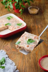 Cold appetizer, sliced meat jellied meat decorated with parsley on a metal spatula on a wooden background.