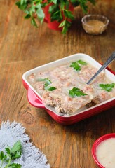 Cold appetizer, jellied meat in a red ceramic form on a wooden background.