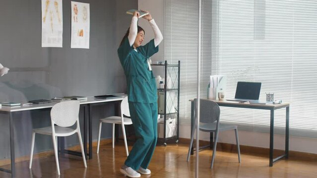 Long shot of happy Asian nurse dancing in clinic after successfully finished internship