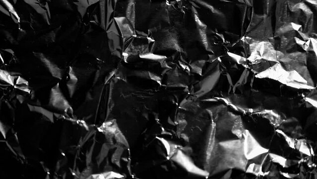 Crumpled foil with glimpses of light and moving shadow along the wrinkles close up