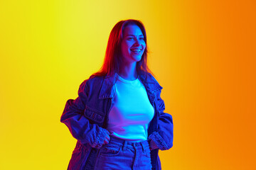 Positive young lady dressed denim casual outfit and posing looking away against gradient yellow-orange background. Gel portrait. Concept of human emotions, self-expression, facial expression, beauty.