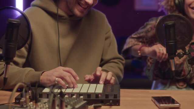 Cropped footage of smiling man creating music on sampler and unidentified lady singing song into microphone and having fun at neon lit home studio at night