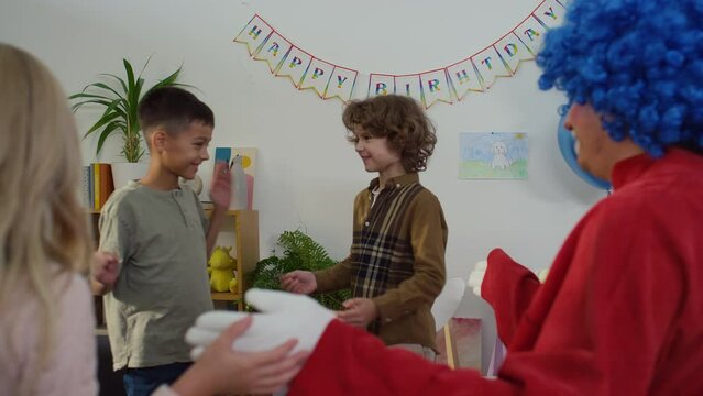 Over shoulder slowmo of 10 yo kids playing funny game with claps together with unidentified clown at birthday party at home. Boy winning and everybody clapping