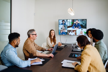 A lively and productive team meeting is captured where colleagues are connected via a large screen, showcasing a blend of in-person and remote collaboration. Virtual meeting concept