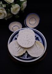 A Thai dessert named Khanom Tuay placed on black background. Thai traditional dessert decorated with flowers and mini ceramic bowls. Thai coconut milk custard. Dessert concept with black background. 