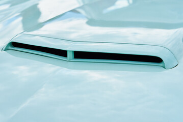 Close-up view of air intake vent on hood of retro sports car, reflecting the bright daylight